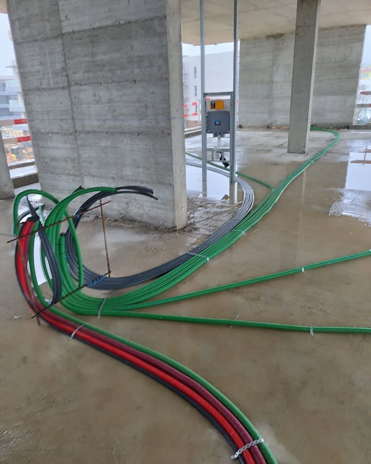 Feixe de tubagem elétrica colorida a atravessar o piso de um edifício, entre pilares de betão