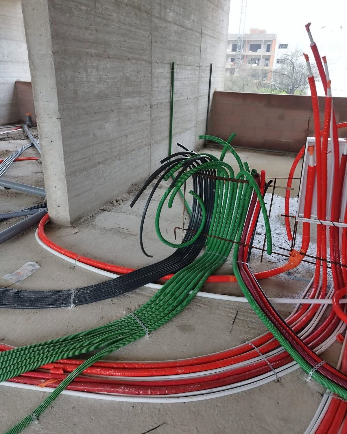 Tubagem elétrica vermelha e verde a subir por um pilar de betão